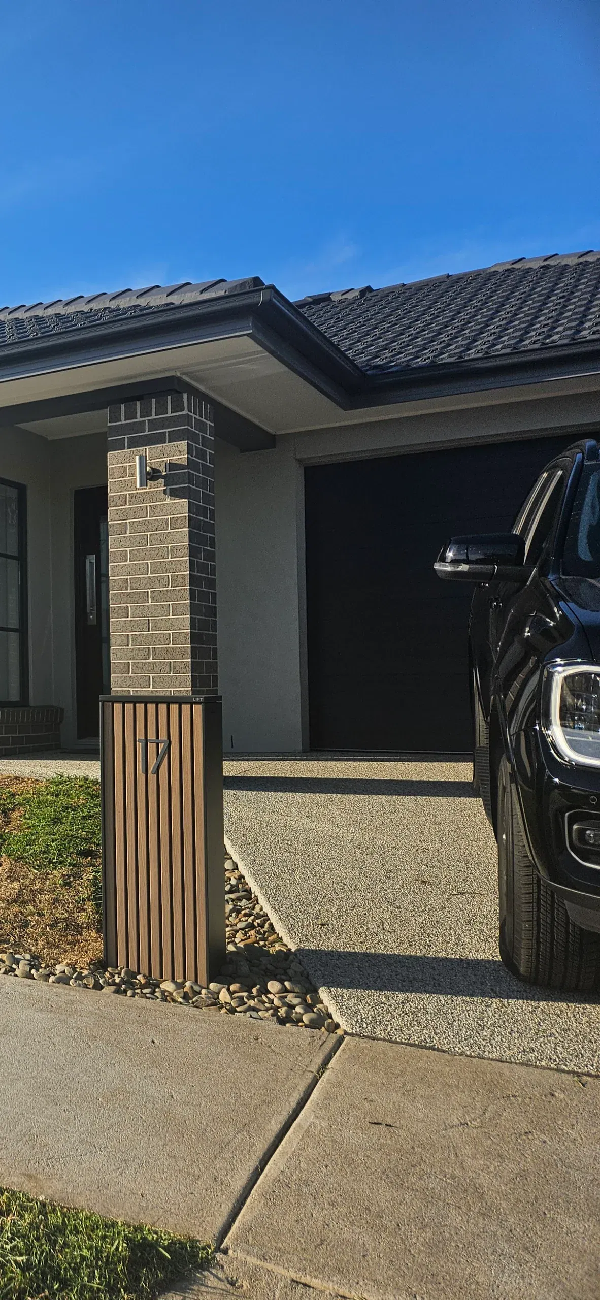 Modern charcoal letterbox with parcel drop set in a pebble bed